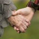 Acercamiento de las manos de una persona joven sosteniendo la mano de un anciano.