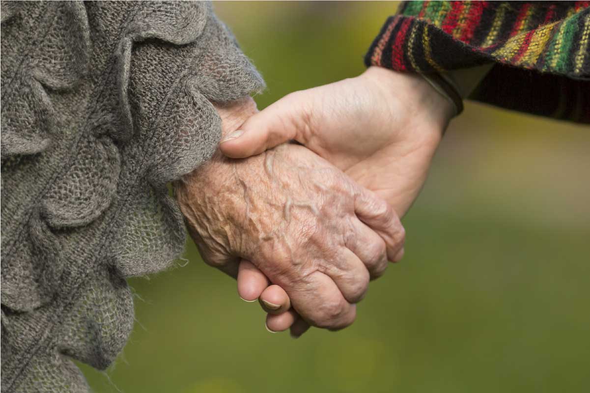 Acercamiento de las manos de una persona joven sosteniendo la mano de un anciano.