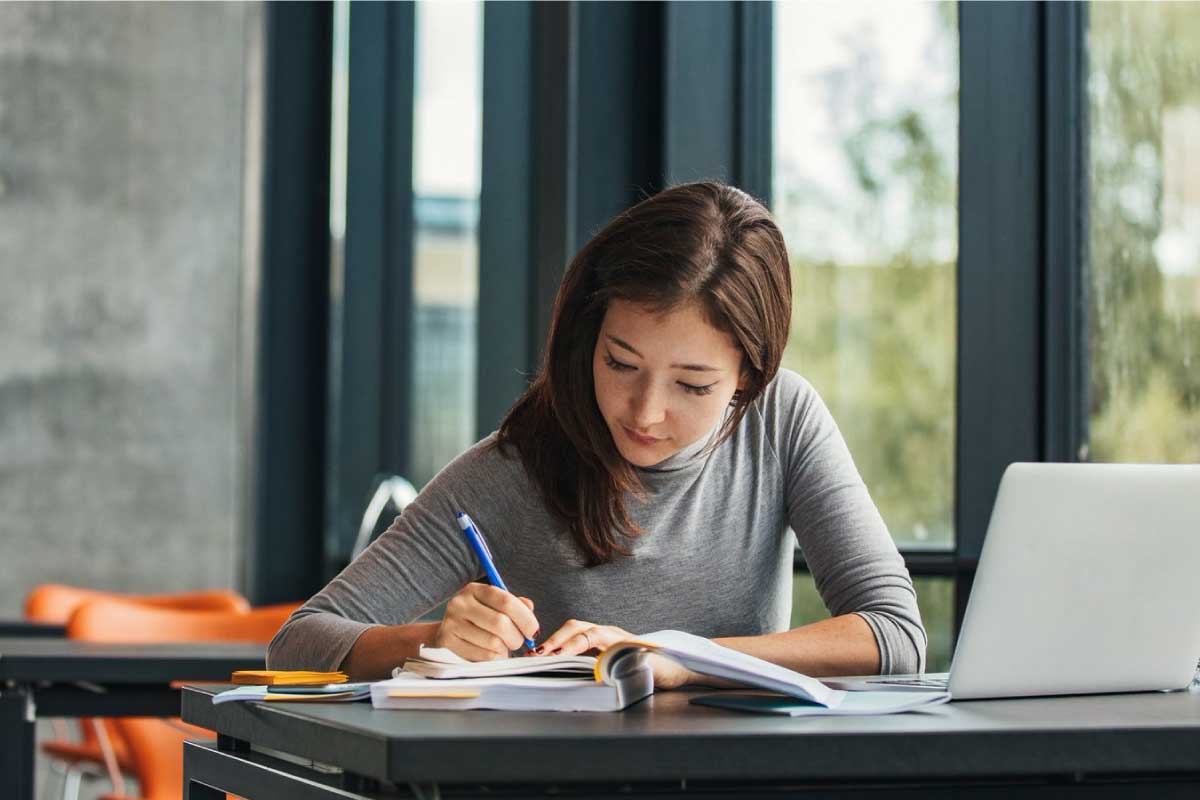 Mujer joven estudiando y tomando nota en un cuaderno