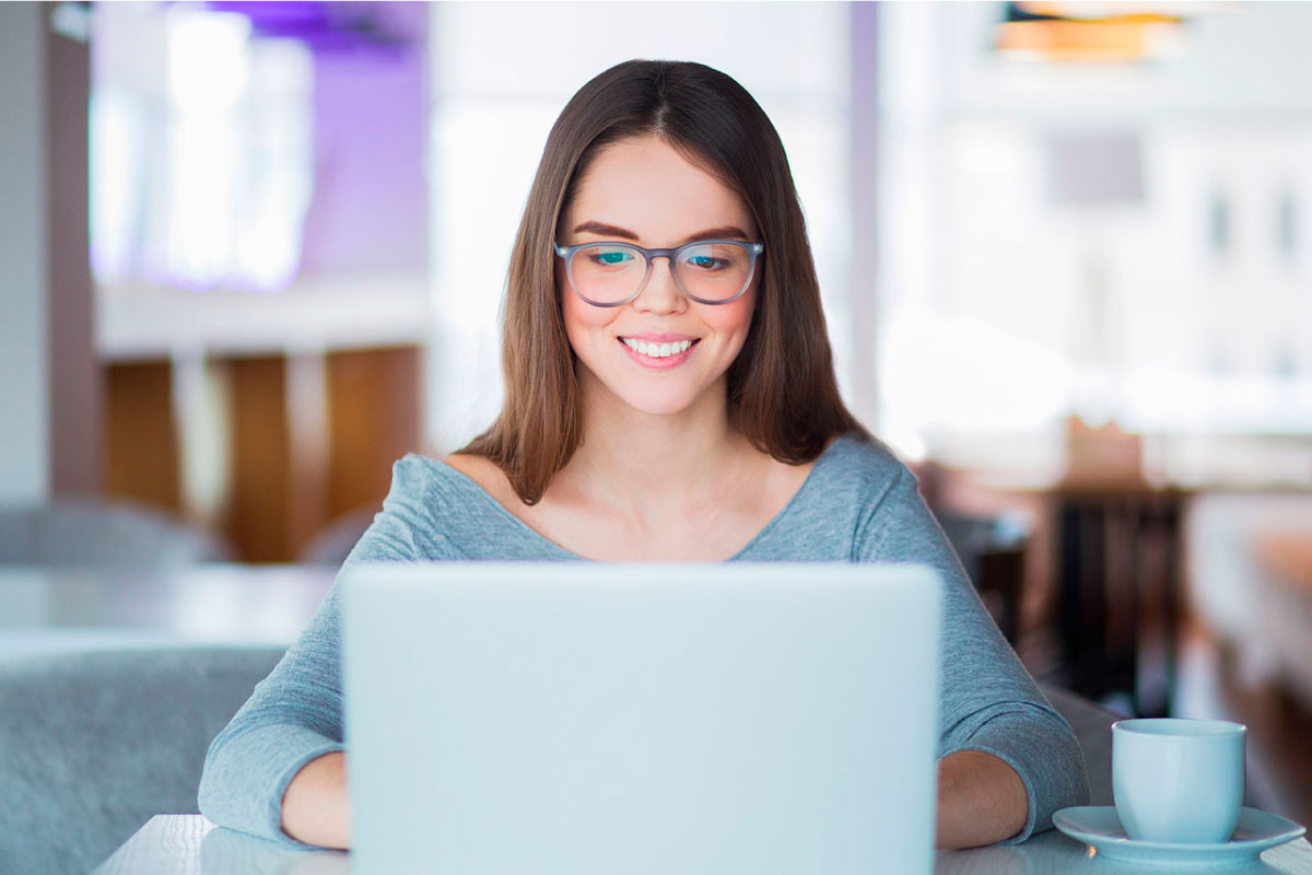 Mujer joven sonriendo, al frente de un computador portatil.