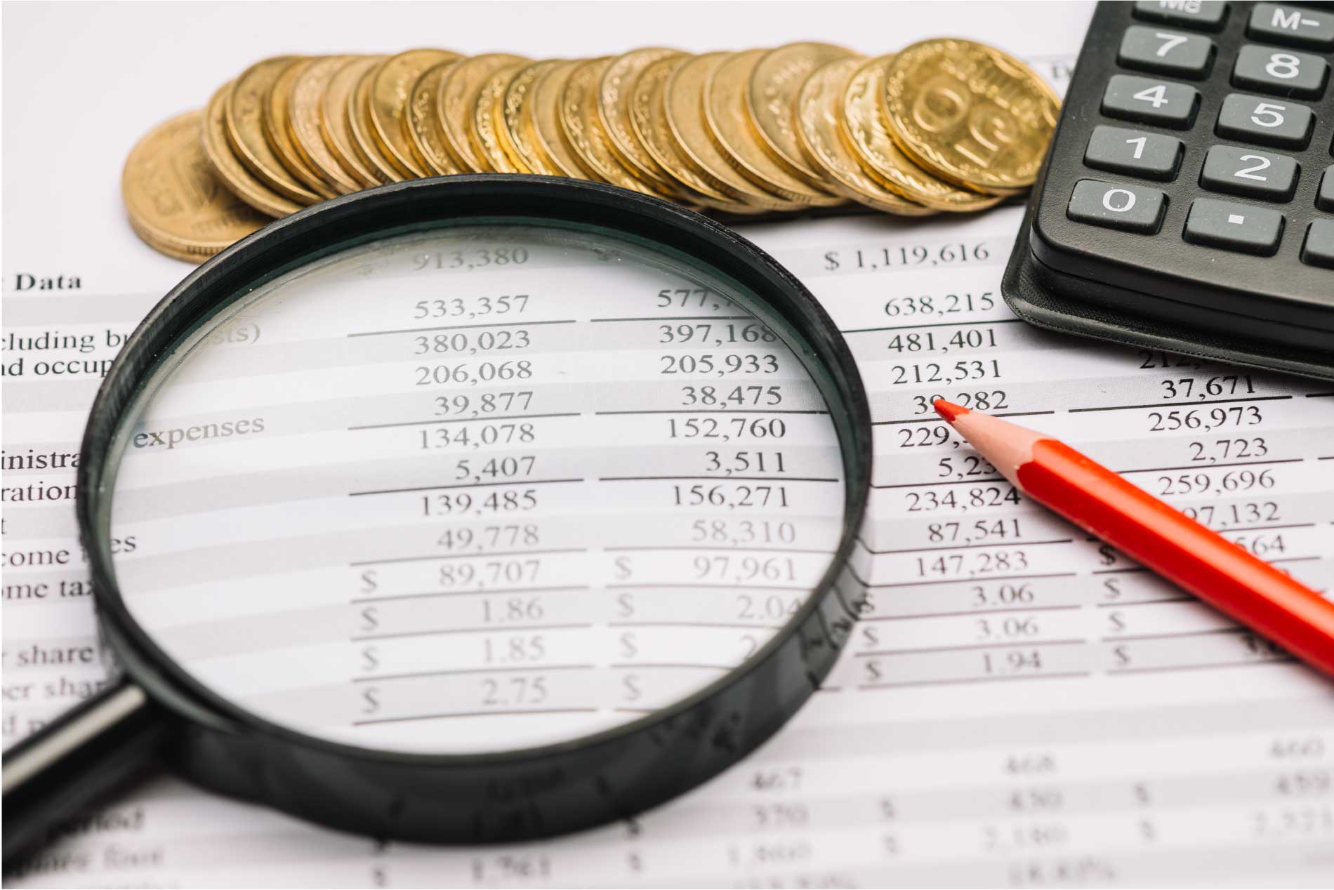 Una lupa, una calculadora y una pila de monedas sobre una hoja de un presupuesto financiero.