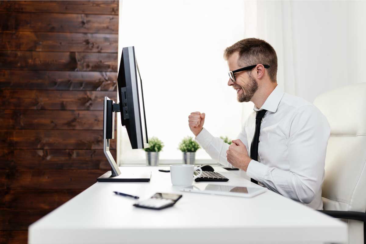 Hombre de negocios frente a un computador con los brazos al frente celebrando