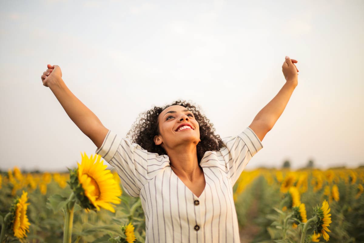 Mujer joven en un campo de girasoles con las manos extendidas hacia el cielo, feliz.