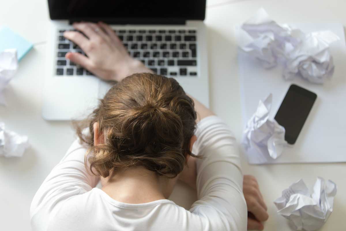 Mujer agotada, con la cabeza sobre su portatil y papeles arrugados sobre el escritorio