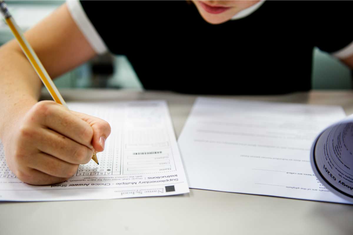 Acercamiento de un joven estudiante presentando un examen, marcando con un lápiz una planilla de múltiples respuestas.