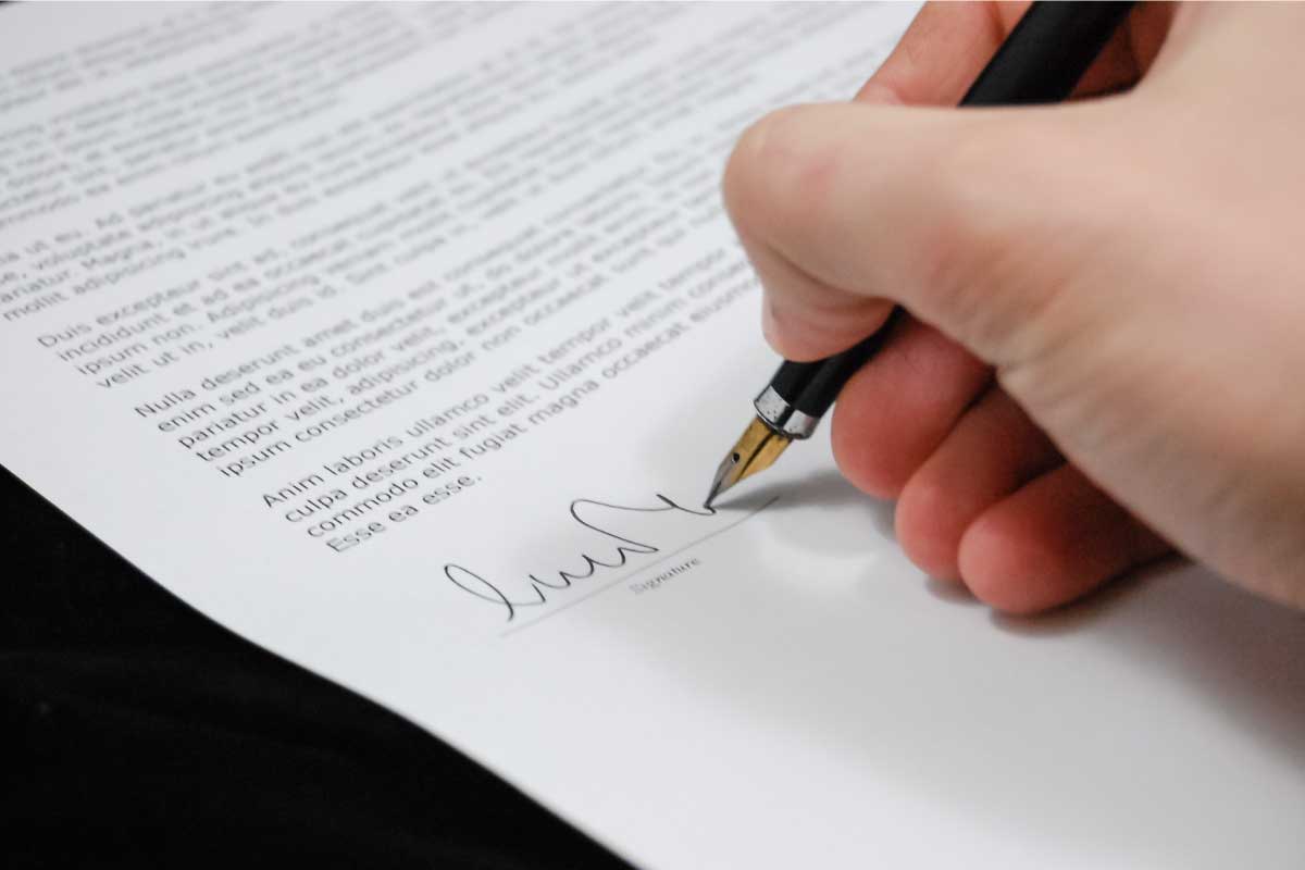 Acercamiento de la mano de una persona firmando un documento con una pluma.
