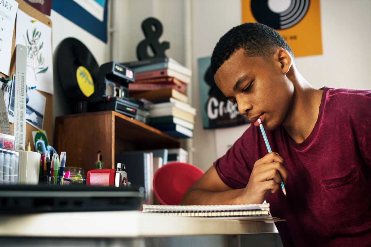 Hombre joven mirando un cuaderno de notas y con un lápiz sobre sus labios, estudiando.