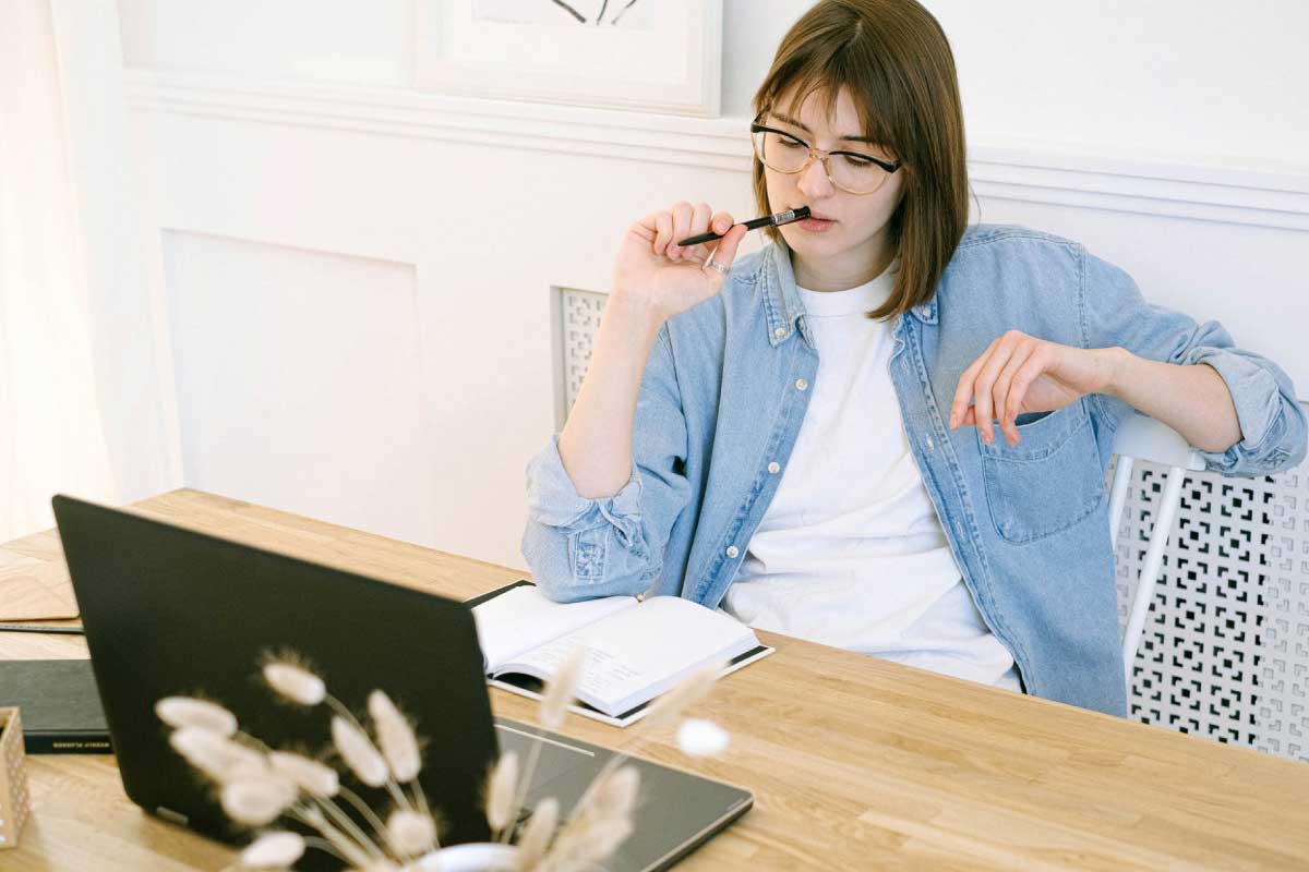 Mujer con actitud pensativa, con un lápiz contra sus labios y al frente de un computador