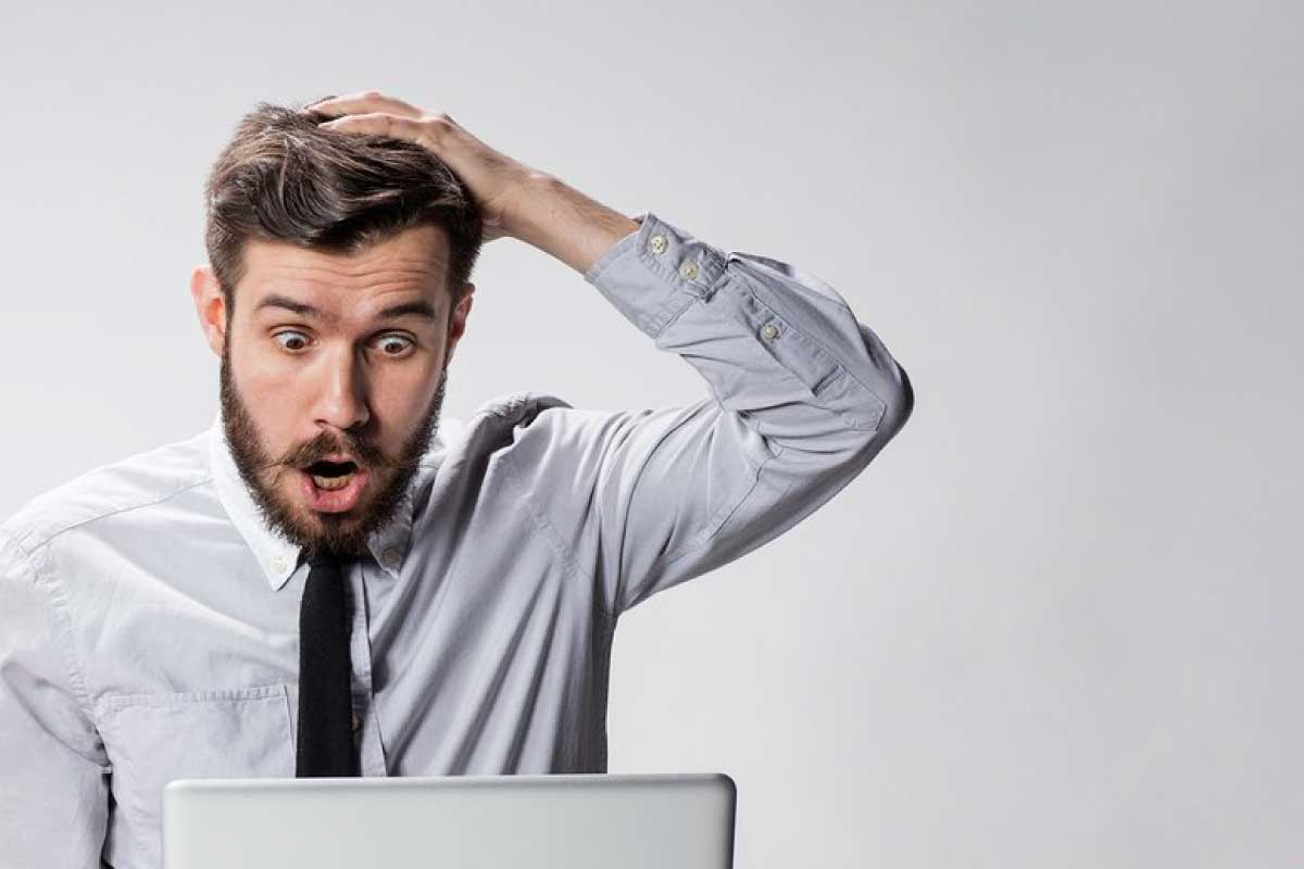 Hombre sentado al frente de un computador con la mano en la cabeza y con expresión de sorpresa.