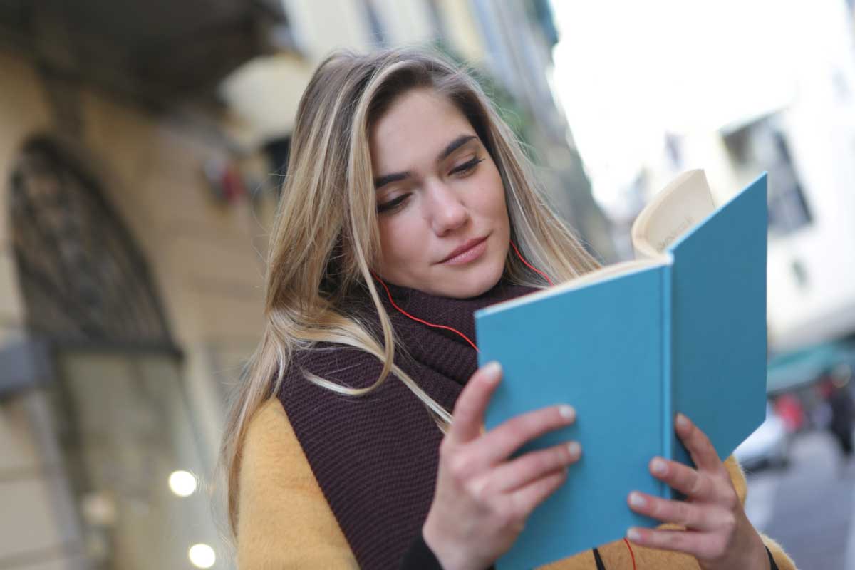 Mujer joven leyendo un libro en exteriores.