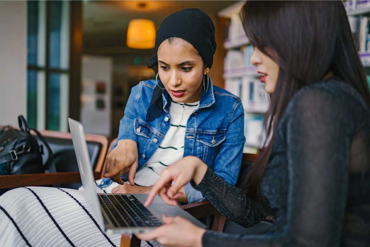 Dos mujeres sentadas, analizando información en un computador portatil.
