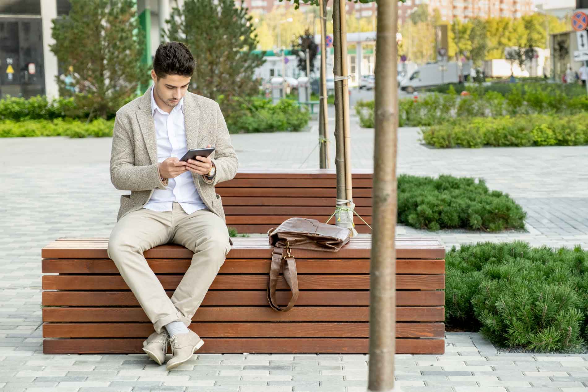 Joven ejecutivo sentado en una banca en exteriores mirando su tablet.