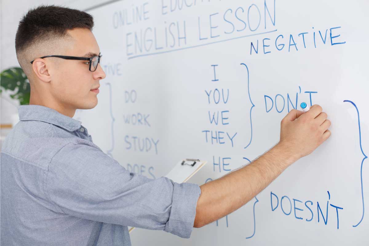 Estudiante escribiendo frases en inglés en un tablero blanco.