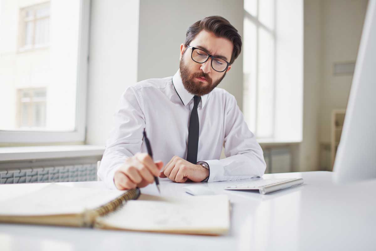 Hombre ejecutivo sentado al frente de un computador tomando notas en un cuaderno
