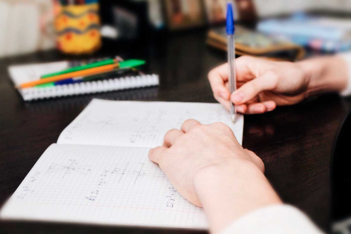 Acercamiento de las manos de un estudiantes haciendo su tarea de matemática en un cuaderno cuadriculado.