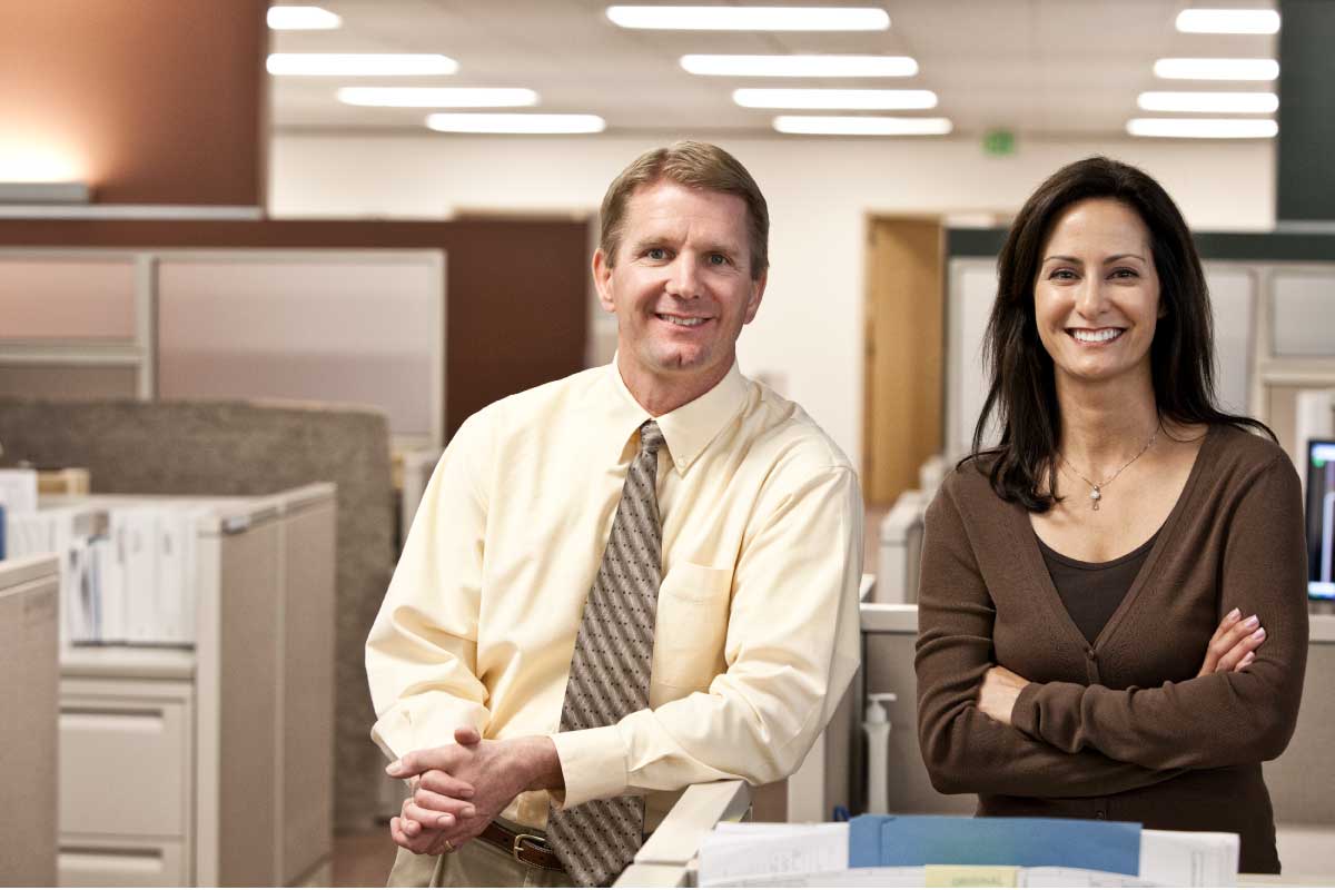 Dos ejecutivos en una oficina sonriendo a la cámara.