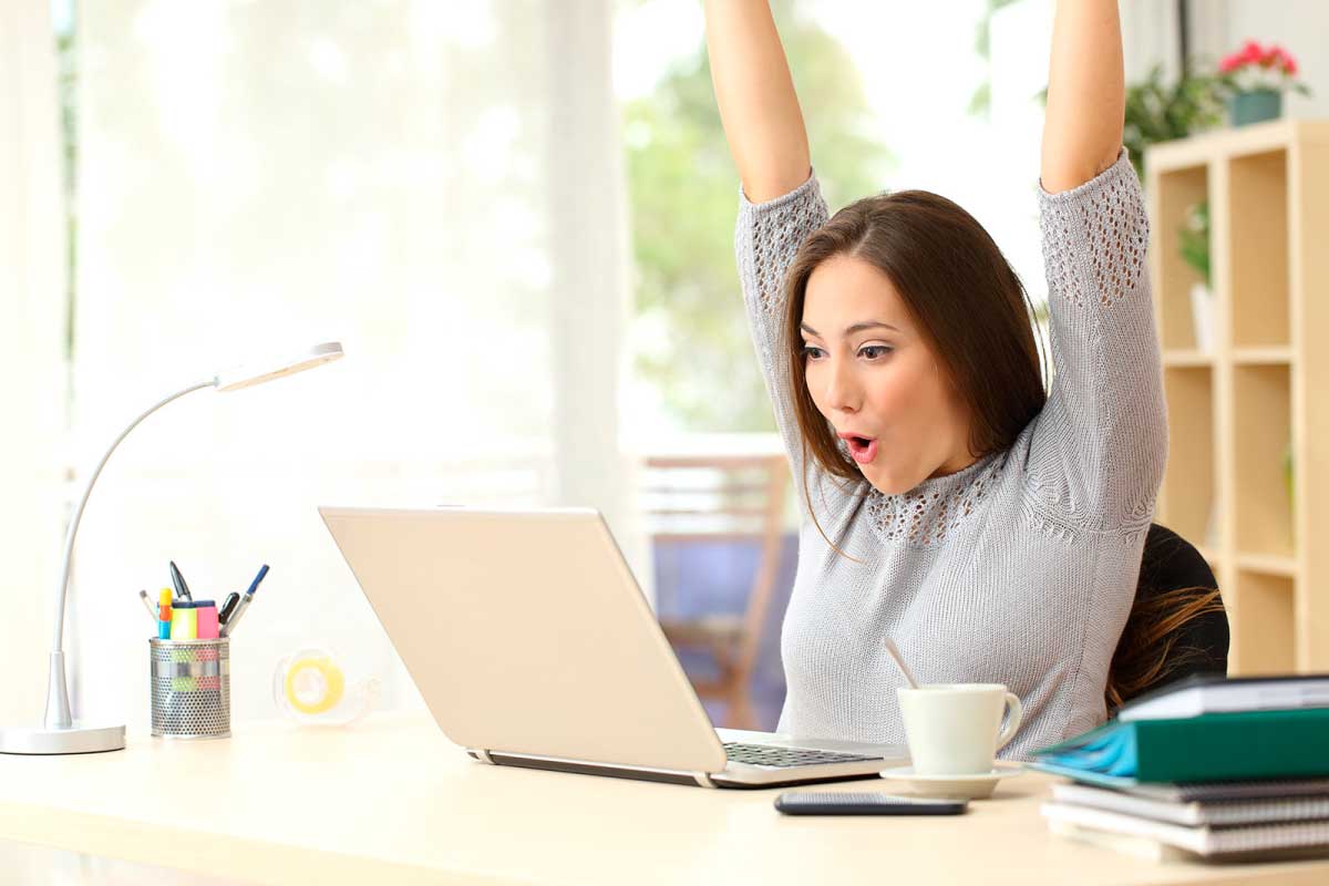 Mujer sentada frente a un computador con los brazos levantados