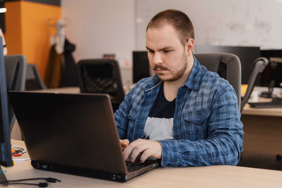 Hombre joven en una oficina, trabajando en un computador portatil.