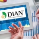 Vista superior de las manos de 2 personas sosteniendo una tableta electrónica con la palabra DIAN y papeles impresos con gráficas.