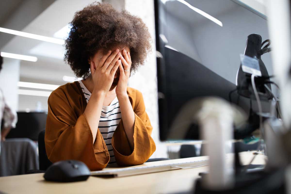 Mujer sentada al frente de un computador con sus manos sobre la cara, frustrada o preocupada.