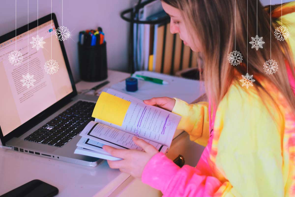 Mujer joven, sentada al frente de un computador portatil, con una libreta de notas en sus manos.