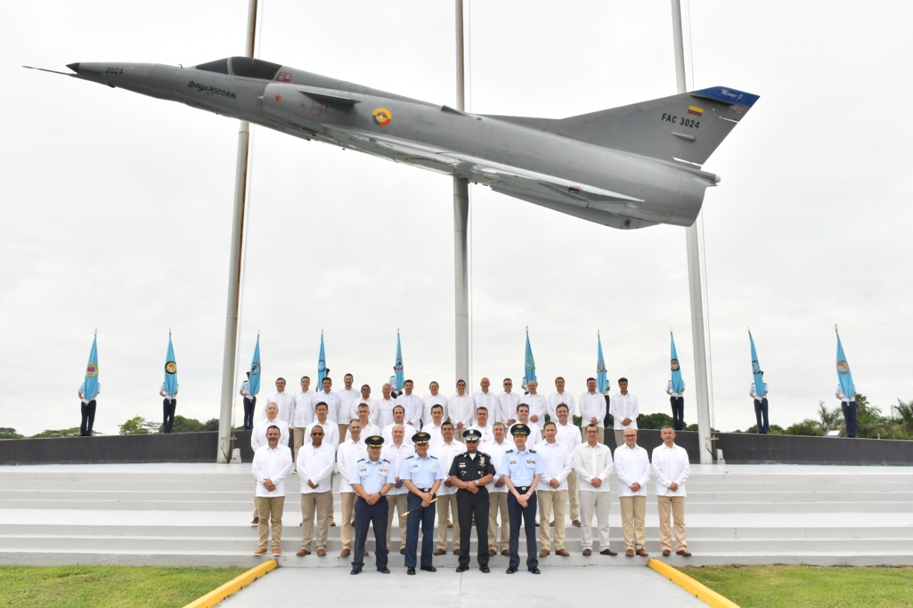 Grupo de militares de la fuerza aérea posando para una fotografía con un avión de guerra en el fondo.