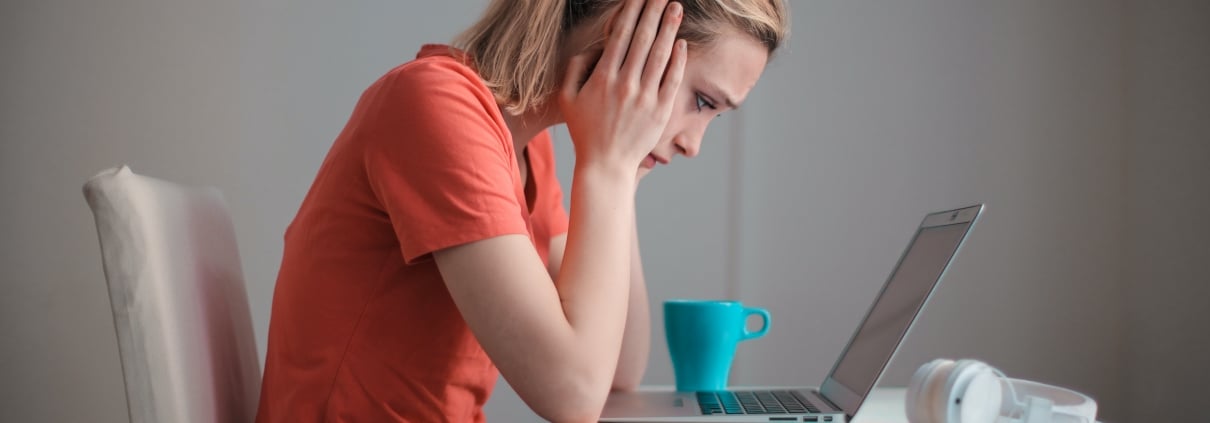 Estudiante sentada al frente de un computador portatil, con sus manos en la cara, mirando atentamente.