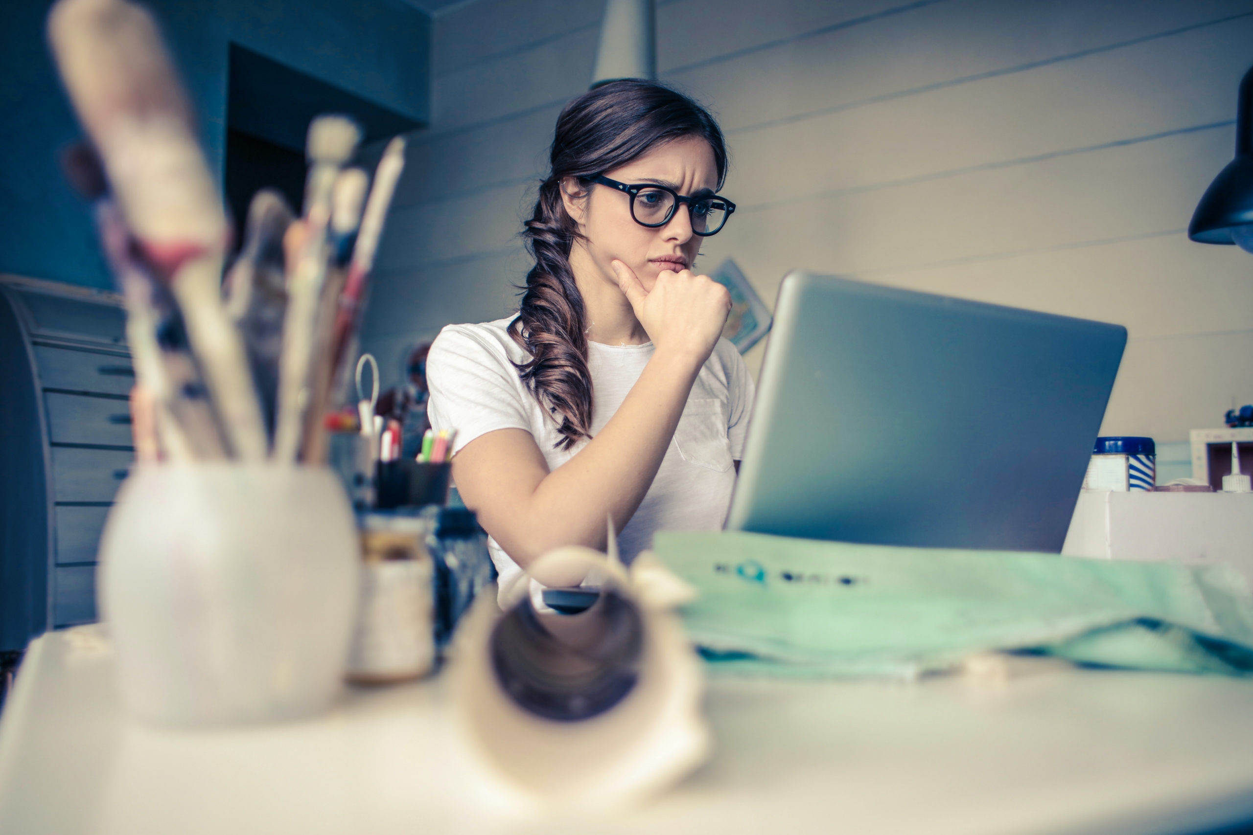 Mujer joven sentada al frente de un computador portatil, con su mano sobre su mentón con expresión de preocupación.