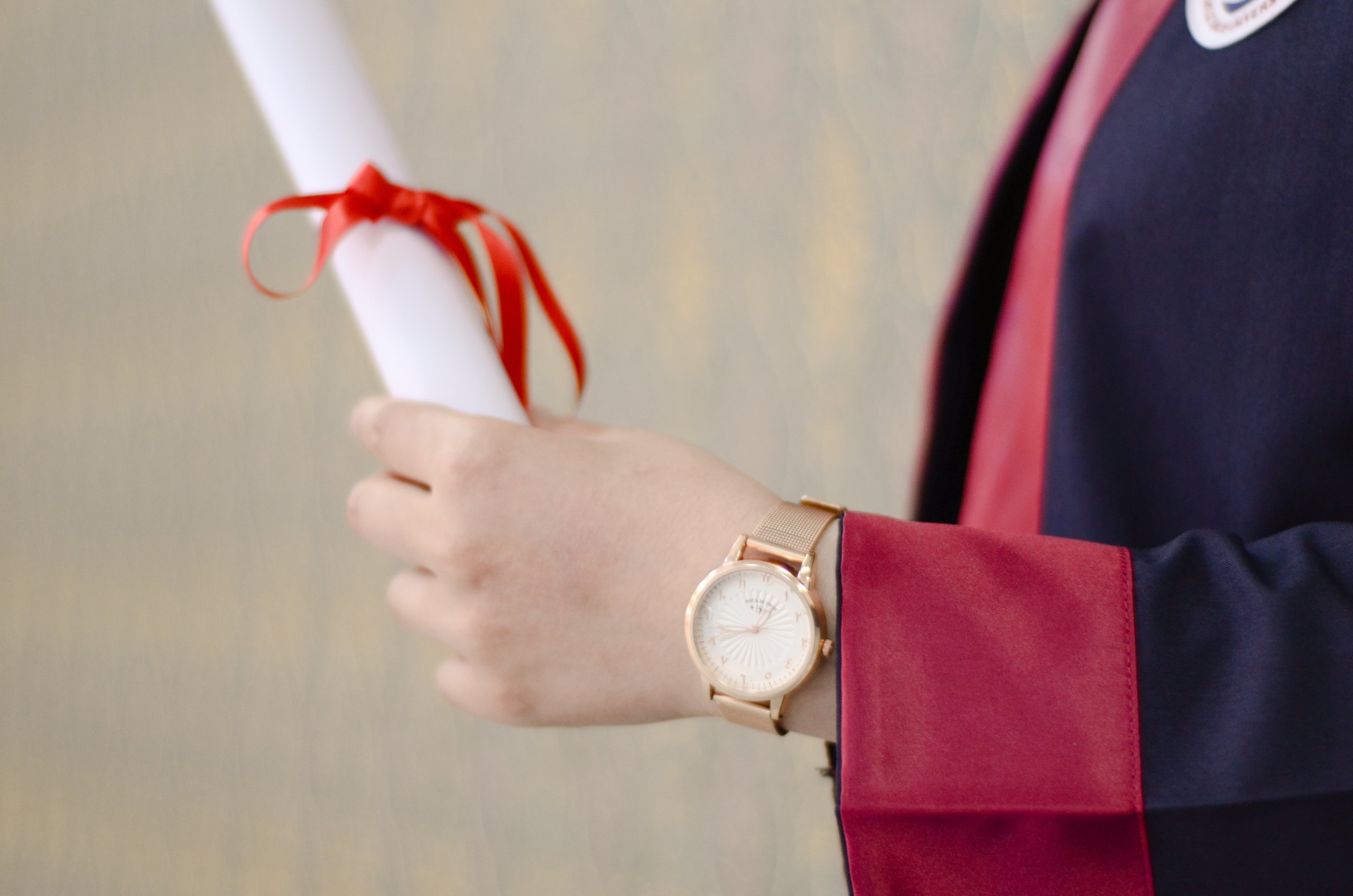 Acercamiento de las manos de un persona graduándose y sosteniendo un diploma.