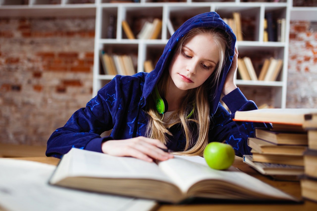 Mujer joven estudiando con un libro abierto sobre un escritorio.