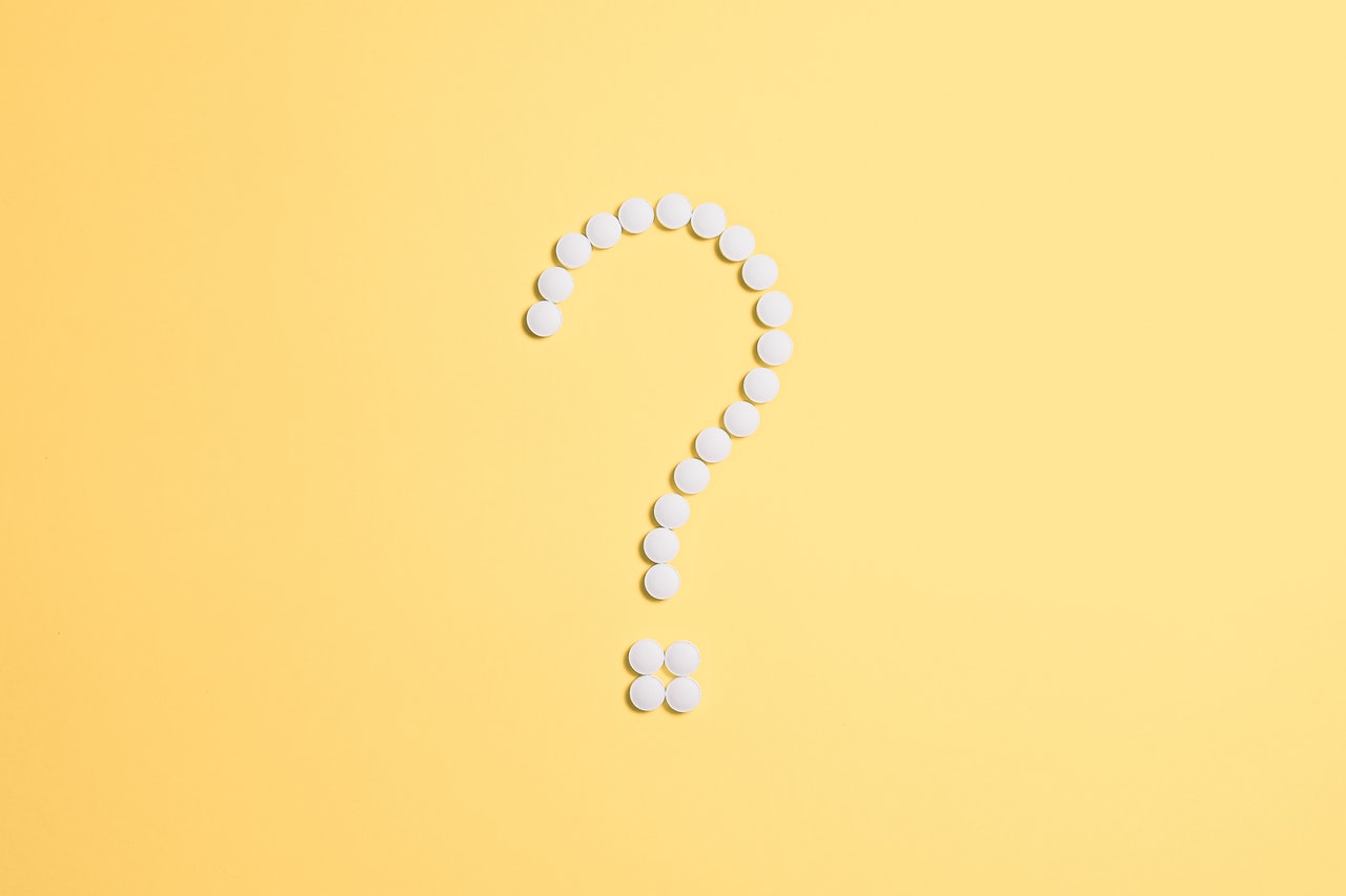 Signo de interrogación formado con píldoras blancas sobre un papel amarillo.