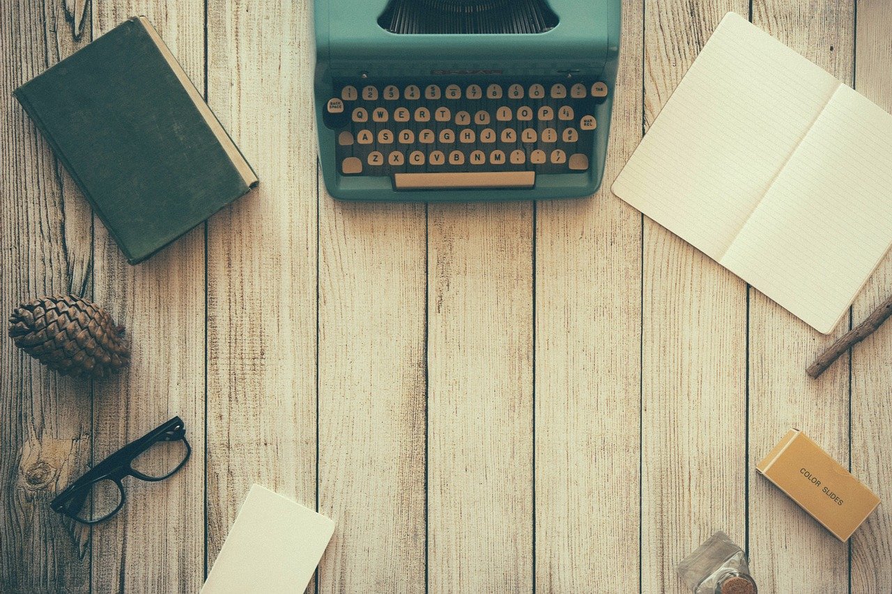 Máquina de escribir sobre un escritorio de madera con una libreta abierta y otros objetos alrededor