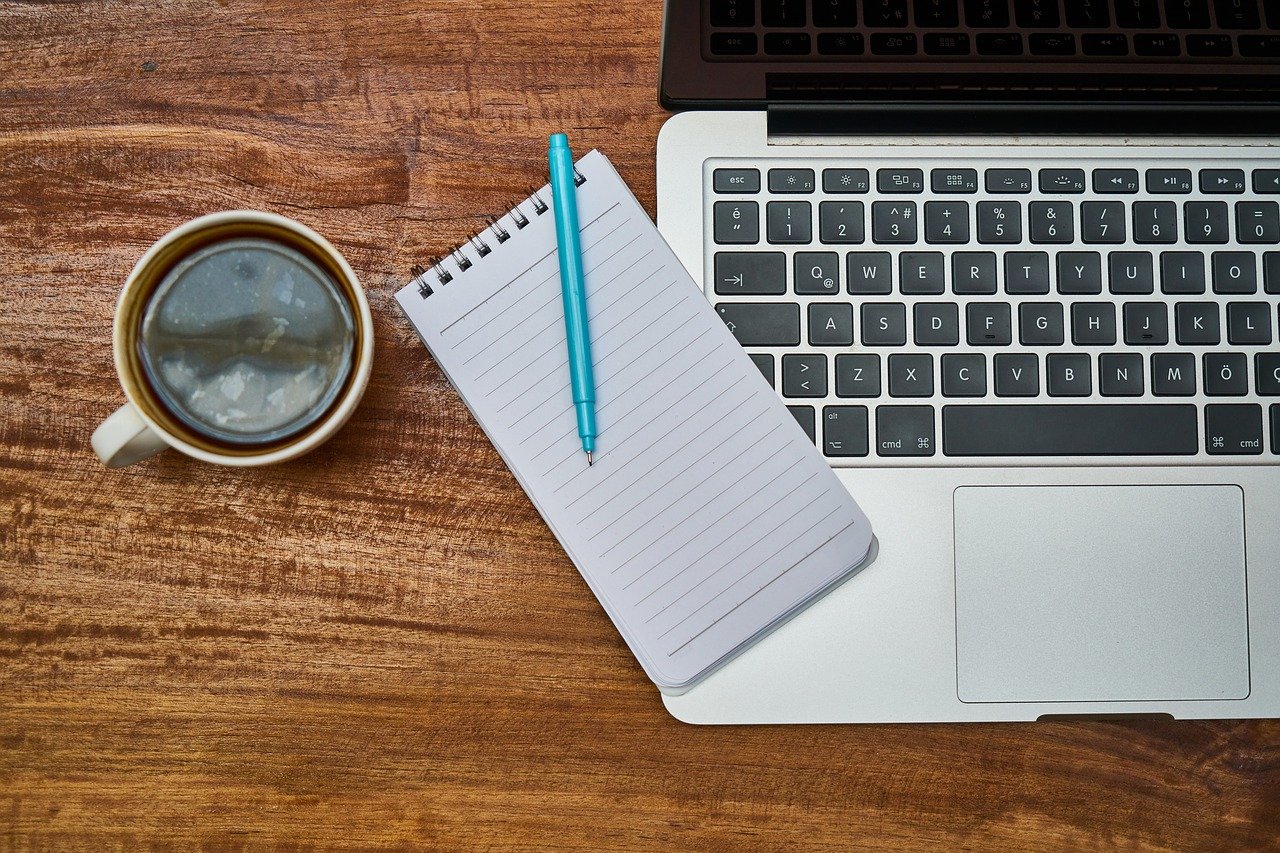 Acercamiento de un computador portatil, una libreta y una taza de café sobre un escritorio.
