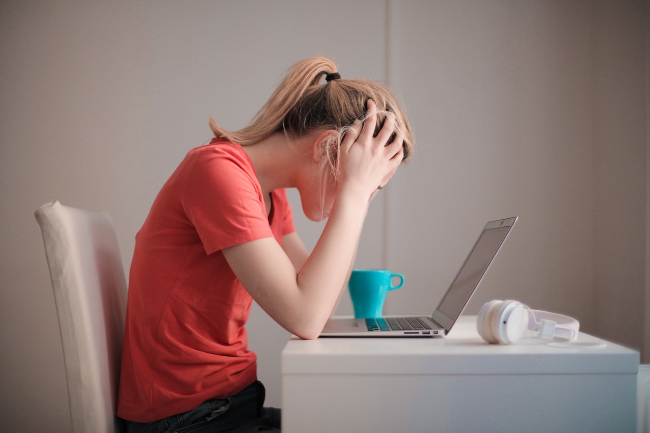 Estudiante sentada al frente de un computador portatil, con sus manos en la cabeza en signo de preocupación.