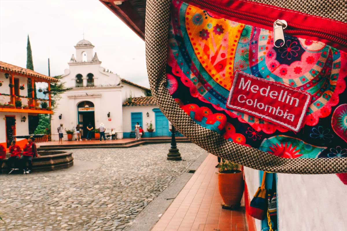 En primer plano bolso artesanal con el texto Medellín, Colombia. En el fondo Iglesia del Pueblito Paisa, Medellín, Antioquia