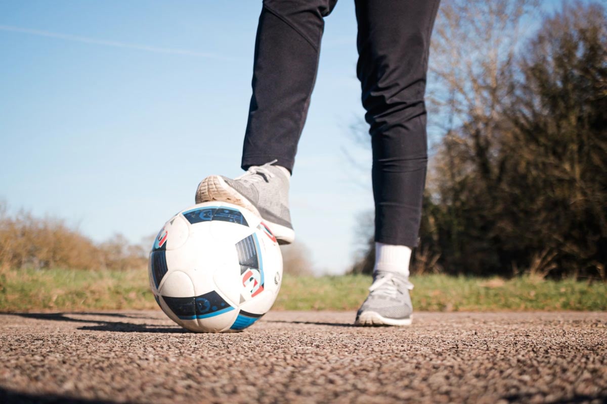 Persona sosteniendo un balón de fútbol entre su pie y el piso, haciendo deporte